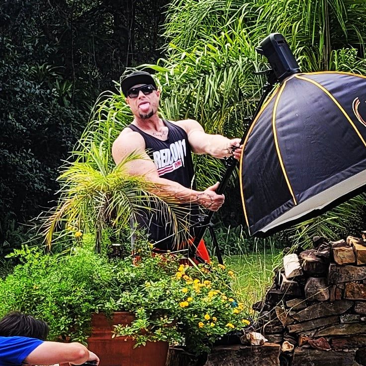 Person setting up lighting equipment and softbox for outdoor photoshoot near tropical plants.