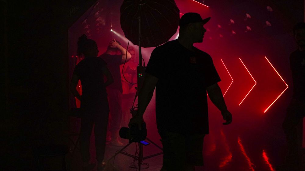 Silhouetted figures on a dark set with red neon lighting and directional arrow designs.