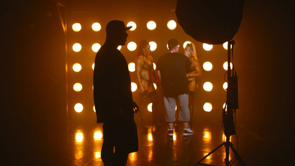 Behind the scenes silhouettes of performers and crew members against a backdrop of warm glowing stage lights.