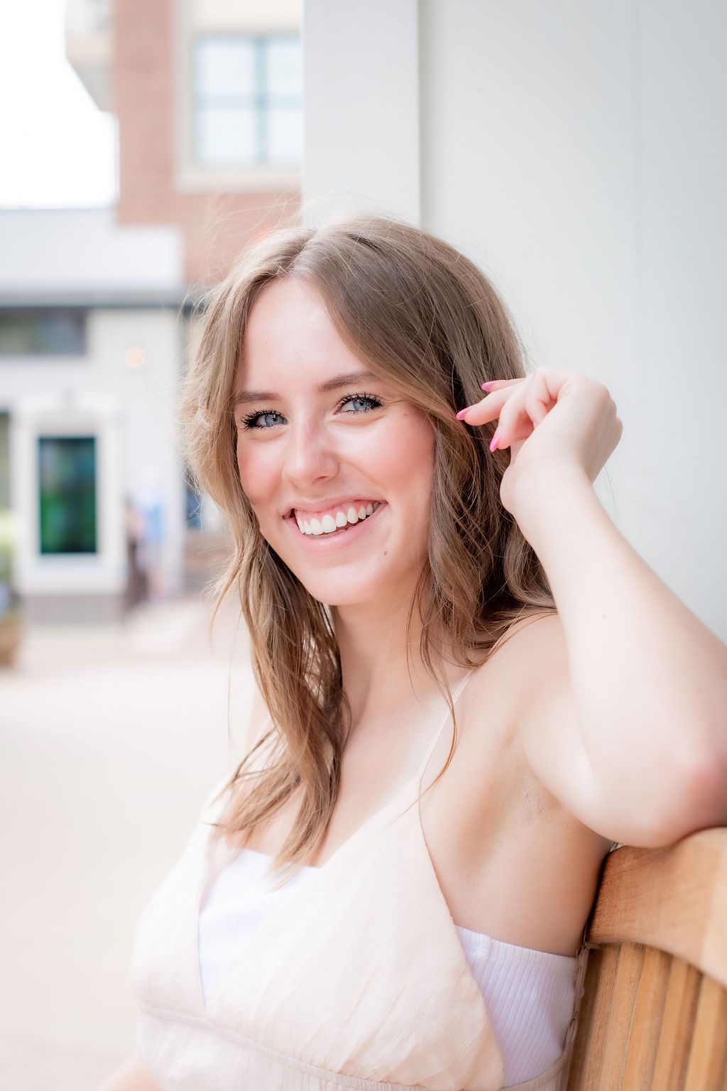 Portrait of woman in white dress smiling while leaning against wooden column outdoors.