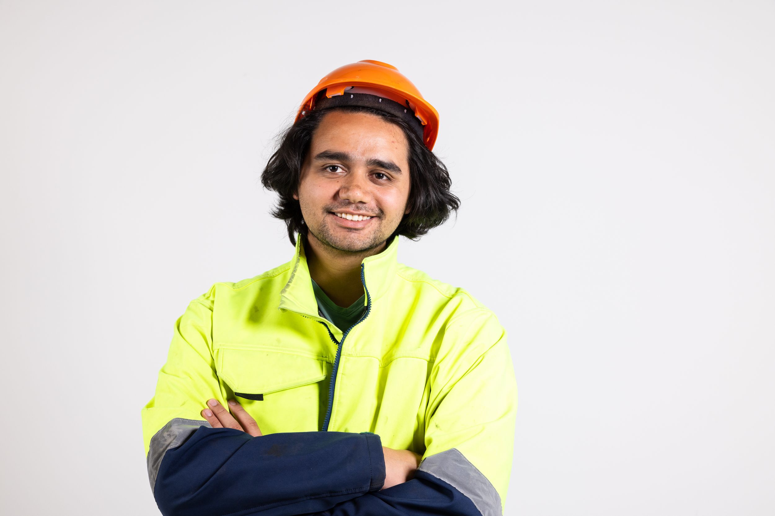 Construction worker in high-visibility gear and orange hardhat smiling against white background.