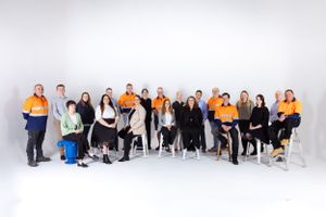 Professional team group photo showing diverse staff members in office and workwear attire against white backdrop.