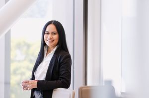 Professional in a black blazer and white shirt standing confidently by a window.