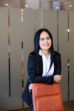 Professional wearing black blazer poses with orange office chair in modern interior.