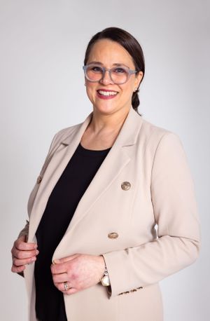 Professional headshot of executive in beige blazer and glasses against light background.