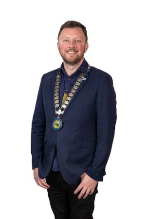 Person wearing formal navy blazer with ceremonial medallion and chain against white background.