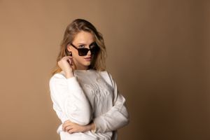 Stylish portrait of someone wearing sunglasses and a white sweater against a neutral backdrop.