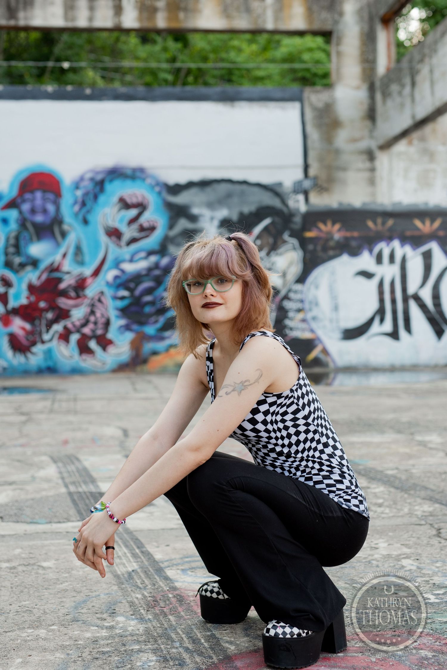 A person in checkered top crouches in front of colorful graffiti wall wearing platform shoes.