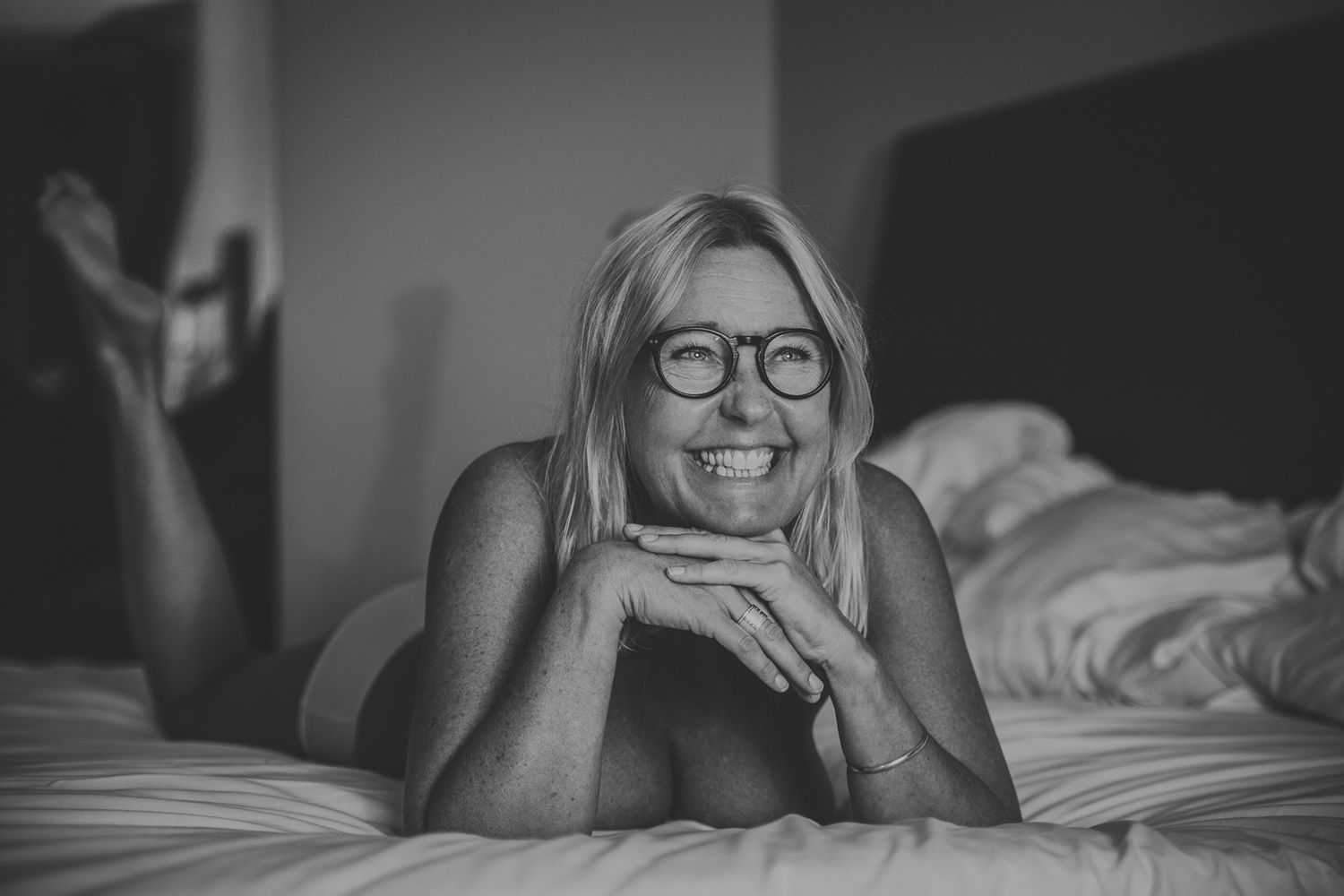 Avklädd kvinna ligger i en säng. Hon ler stort. Budoirfotografering på Hotell 11 i Göteborg.