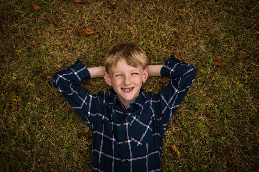 A sequence of seven photos showing someone jumping and playing in fallen autumn leaves while wearing a navy plaid shirt.
