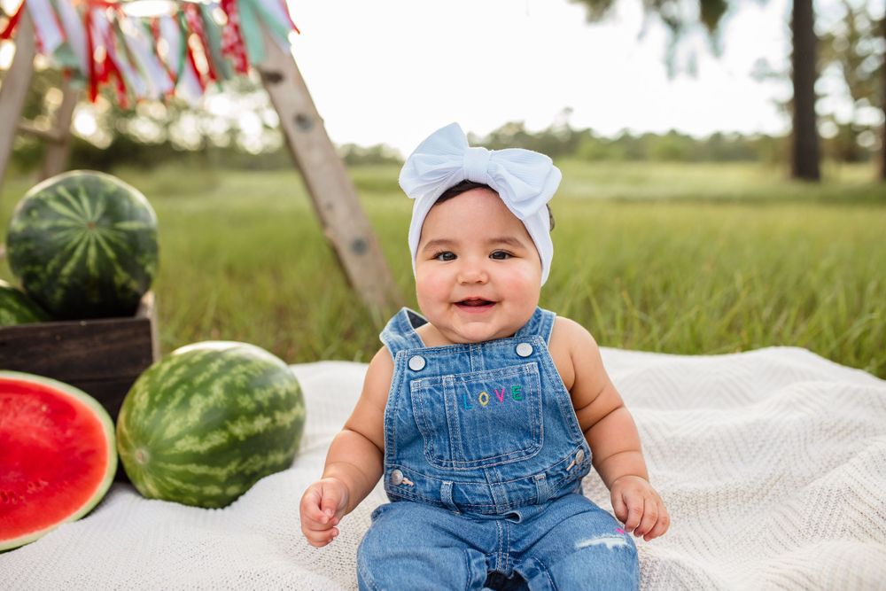 A collection of summer photos showing a baby in denim overalls enjoying watermelon and outdoor activities on a blanket.