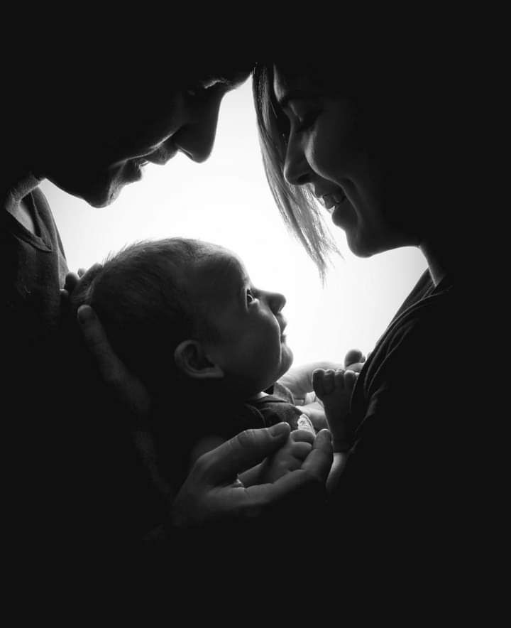 Silhouette of parent and baby in tender moment against bright background.