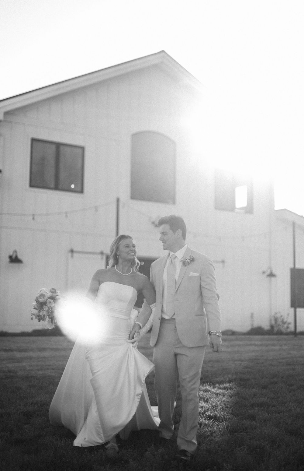 A couple walks together at sunset outside a white building on their wedding day.