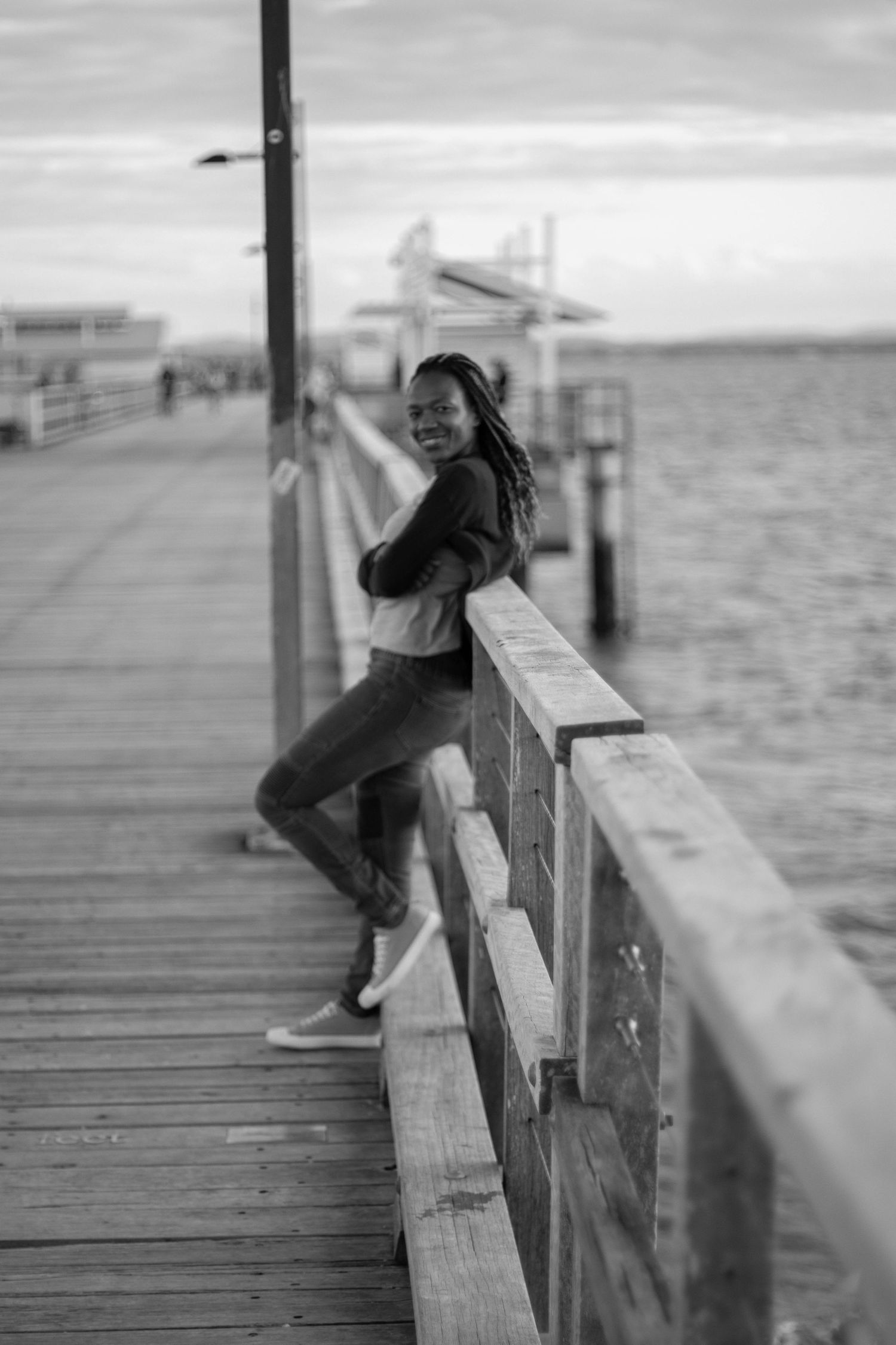 Black and white photo of joyful person posing on wooden pier by the ocean.