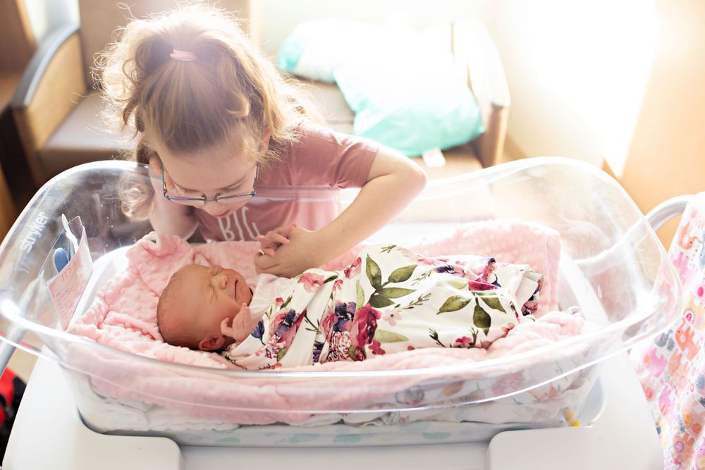 New baby sleeping peacefully in a hospital bassinet with floral swaddle blanket.