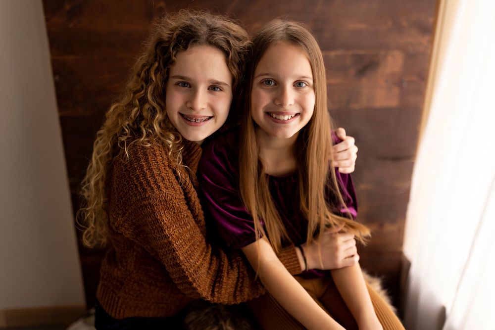 Two friends in cozy sweaters sharing a warm embrace against wooden wall background.