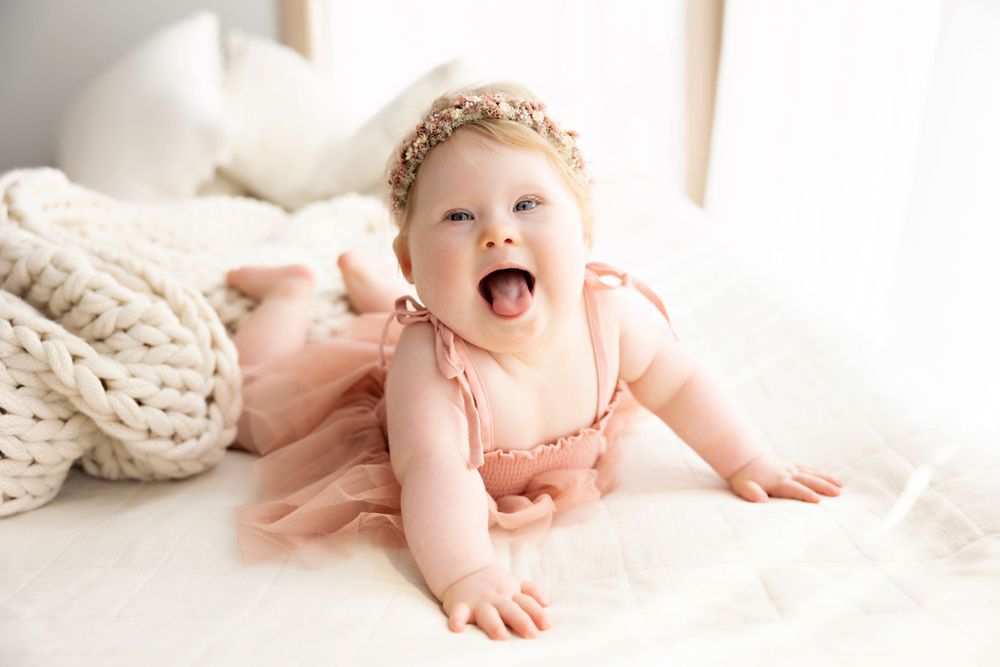 Happy baby in pink tulle dress crawling on white knit blanket.