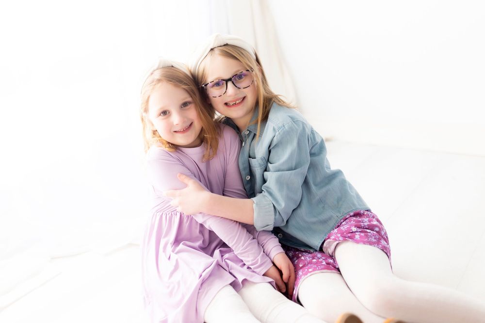 Two children in casual attire sitting together and embracing on a bright white background.