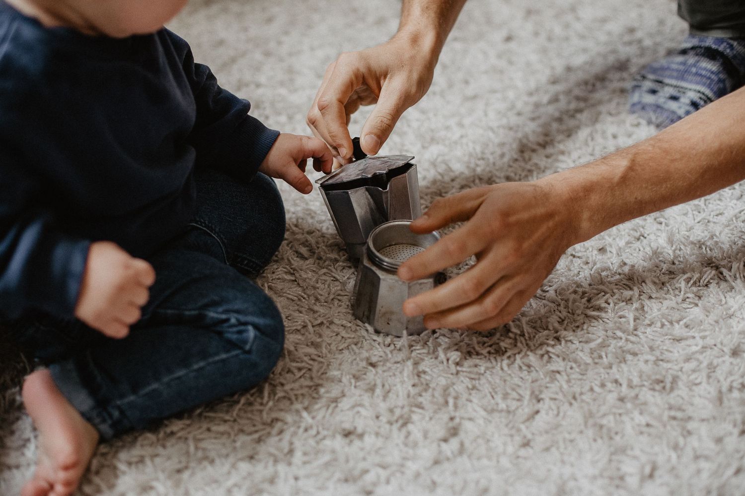 Erwachsenenhände, die Kinderhänden helfen einen Espressokocher auf dem Teppich zu öffnen.