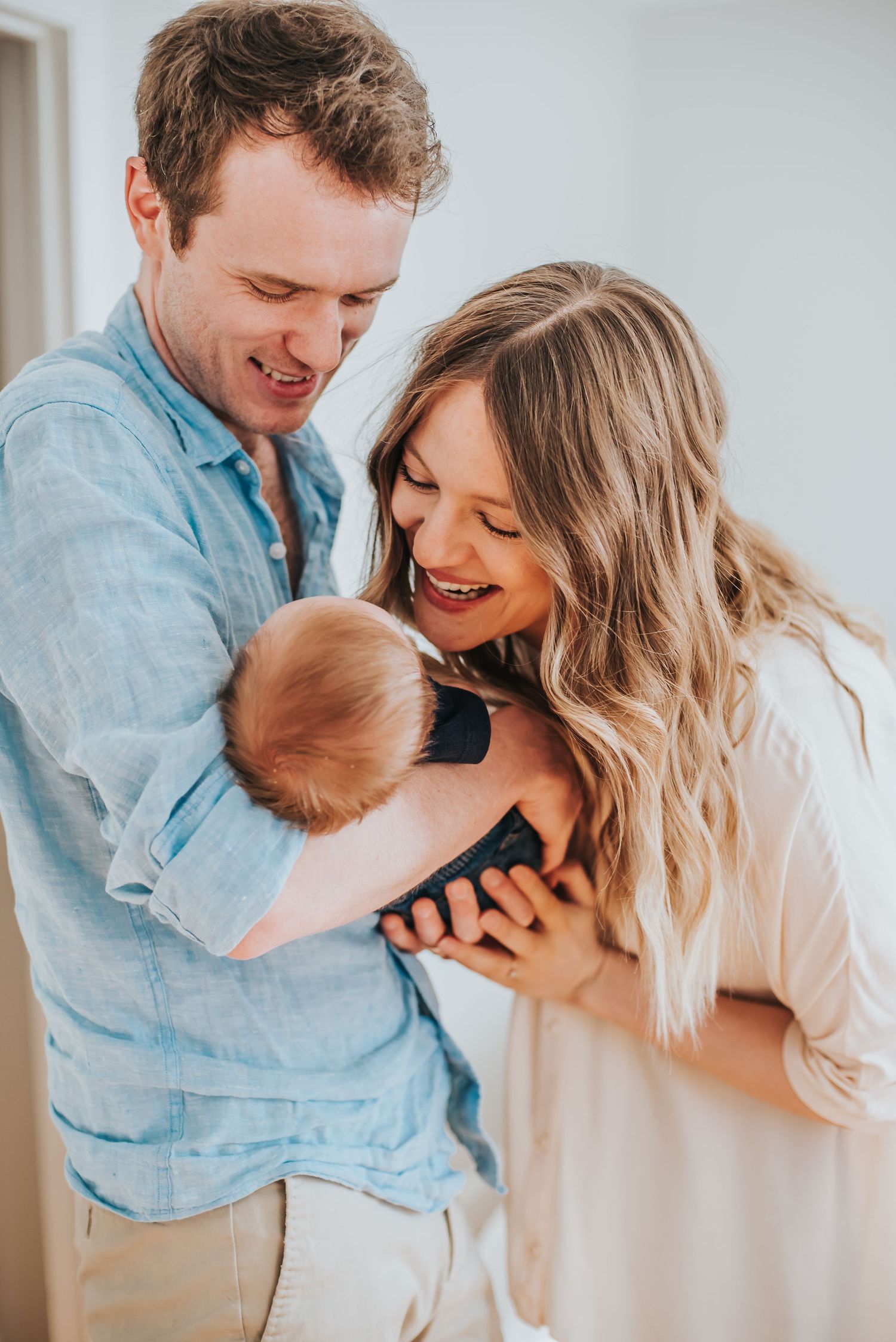 Caucasian newborn being held by their parents as they stand and look at him.