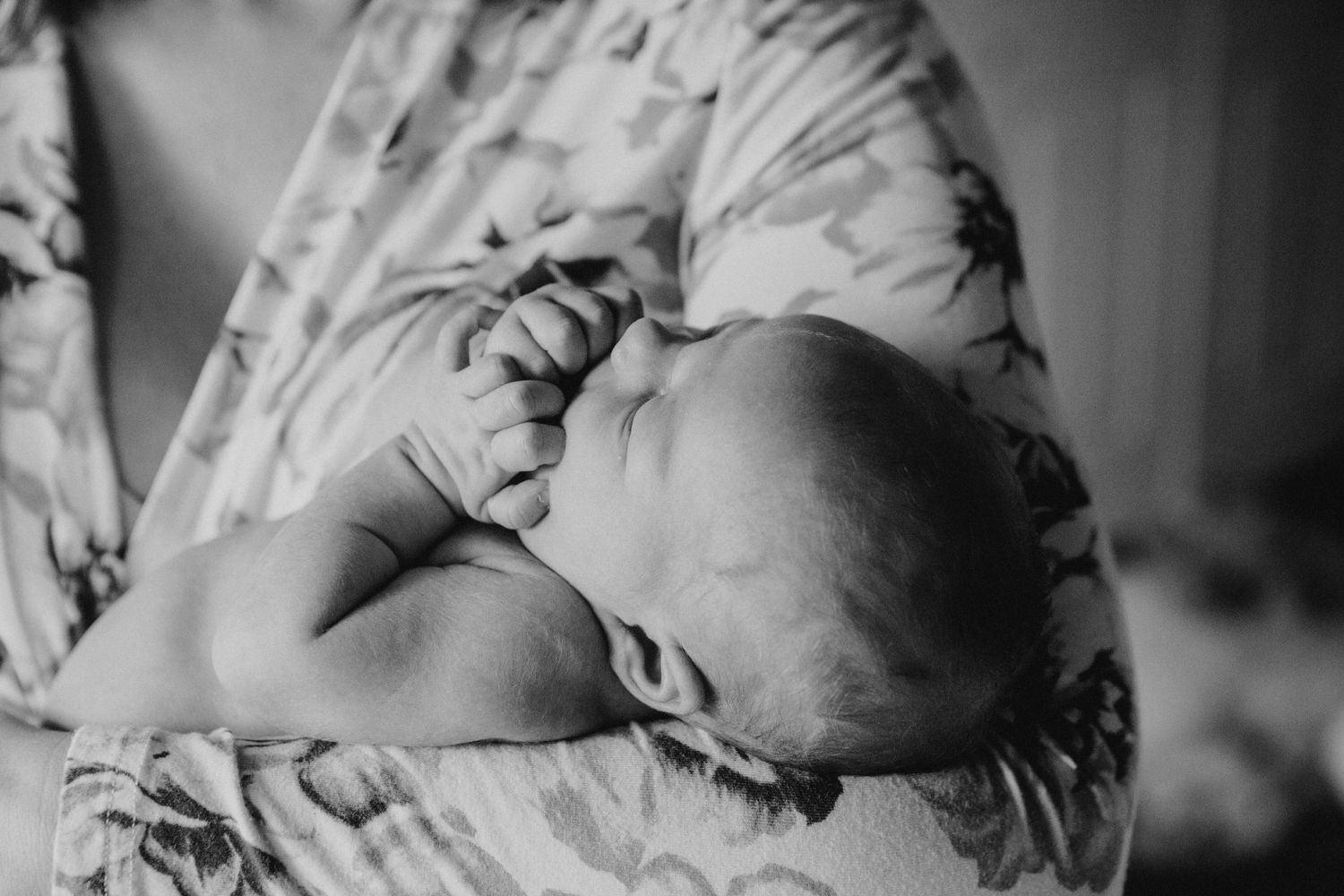 A tender black and white portrait of a sleeping infant swaddled in floral fabric.