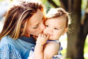Mother and baby girl daughter kissing for an outdoor lifestyle photo.