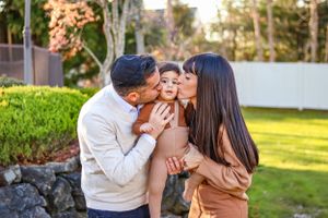 Parents kissing their little baby at their backyard photoshoot.