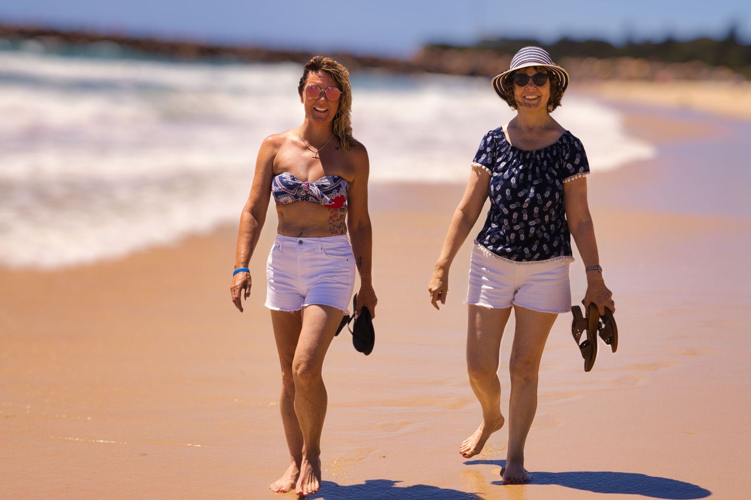 two woman walking along a beach on a sunny day