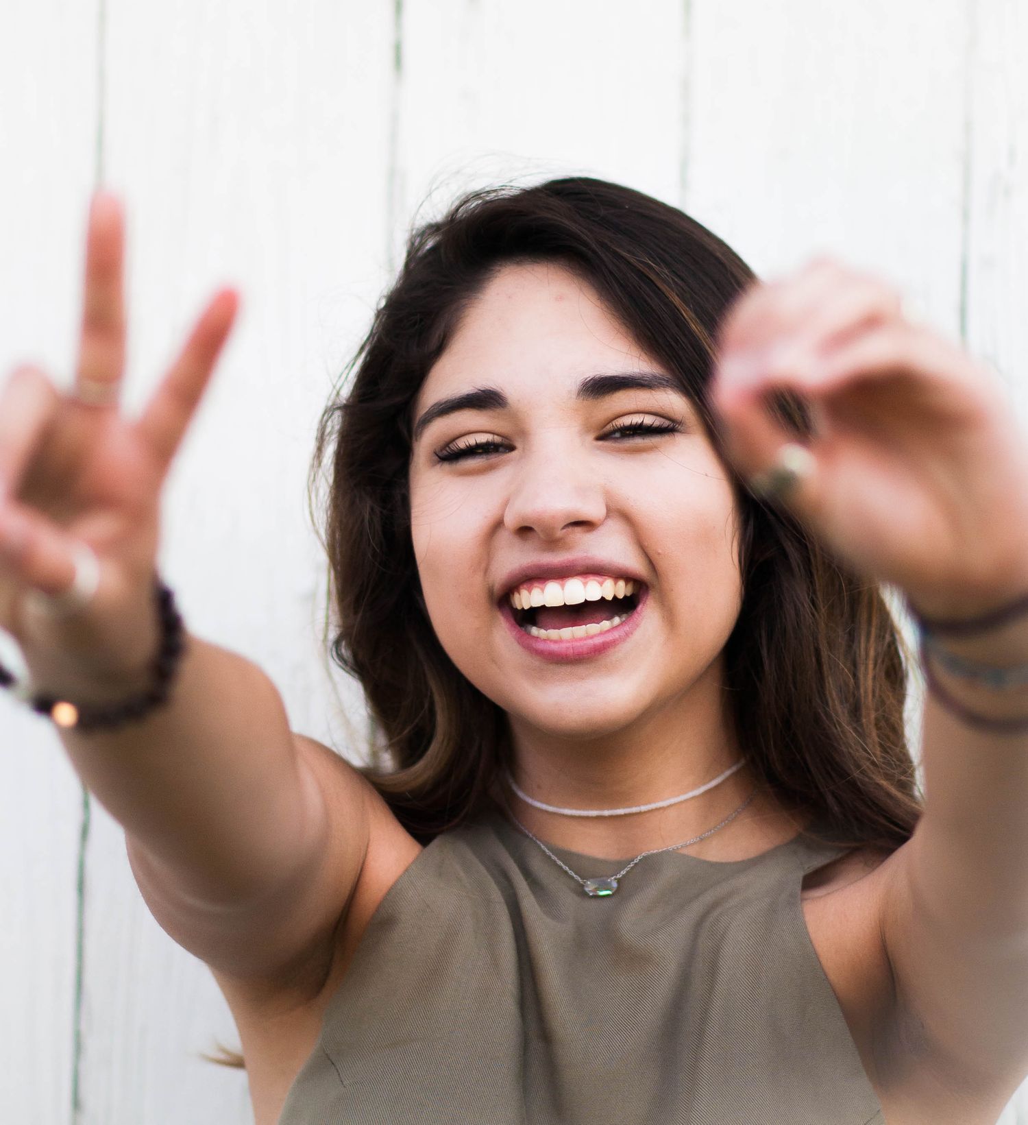 Happy young woman making peace signs with both hands laughing against a white background.