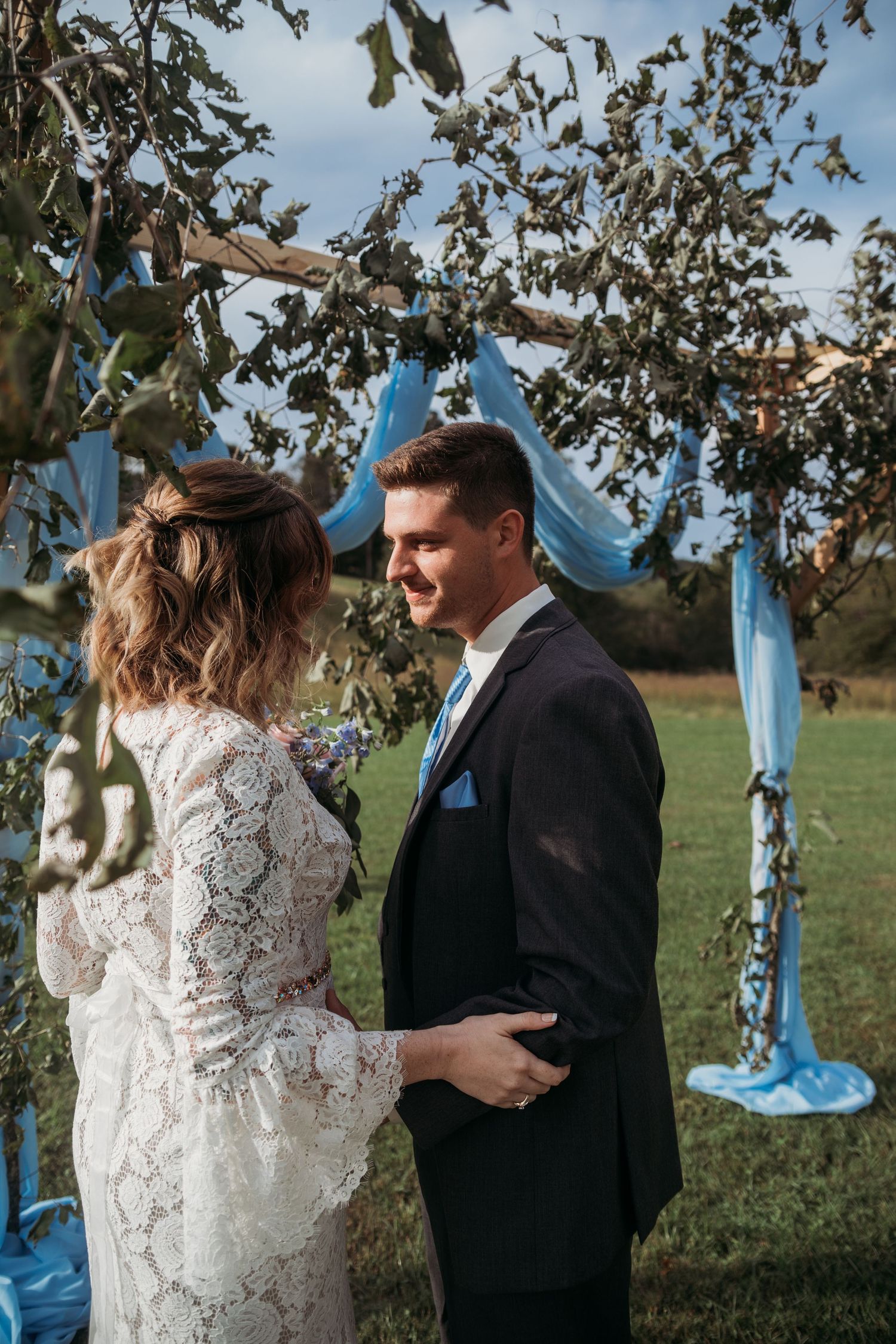 A romantic outdoor wedding scene with blue fabric draping and natural greenery decorations.