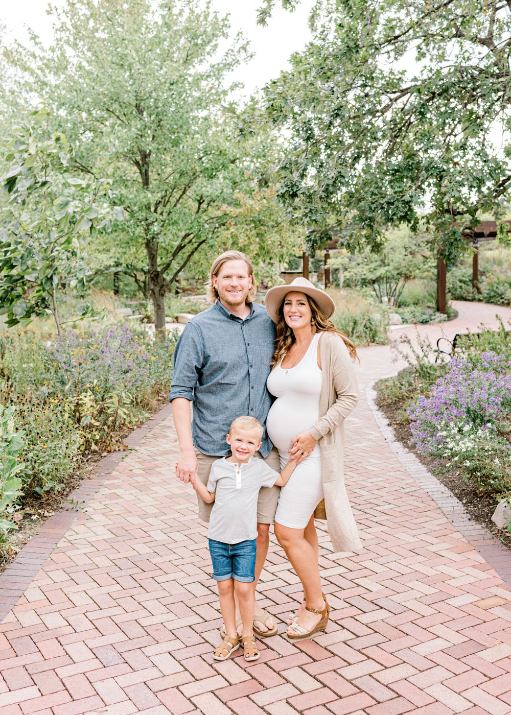 Family maternity photo on brick pathway surrounded by flowering garden.