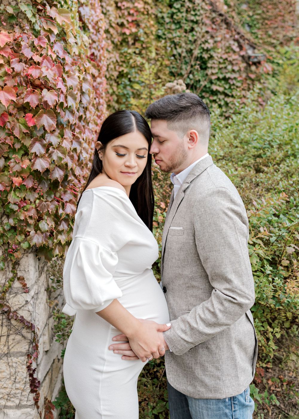 Maternity portrait with couple against ivy-covered wall in autumn.