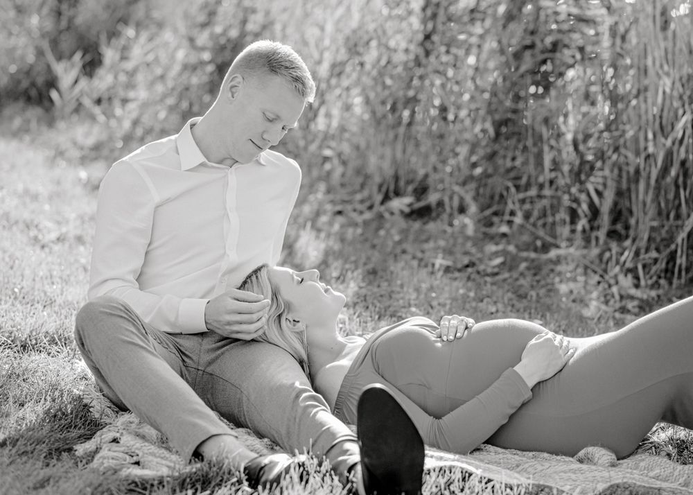 A romantic black and white portrait of a couple laying in grass during sunset.