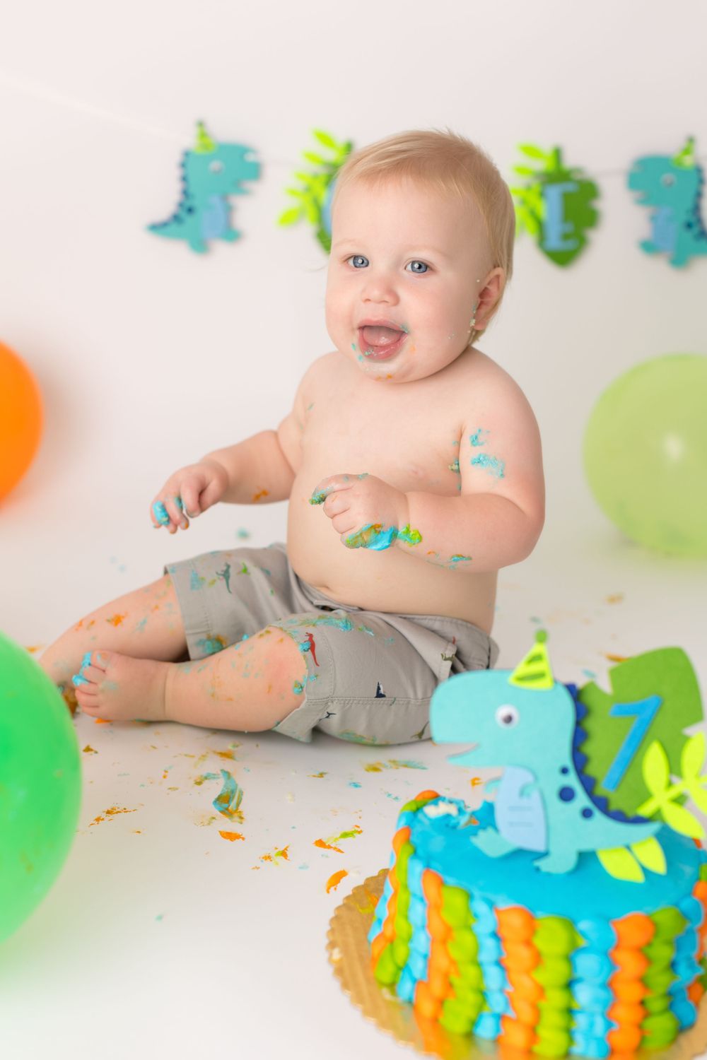 Excited baby covered in cake frosting with dinosaur-themed birthday decorations.
