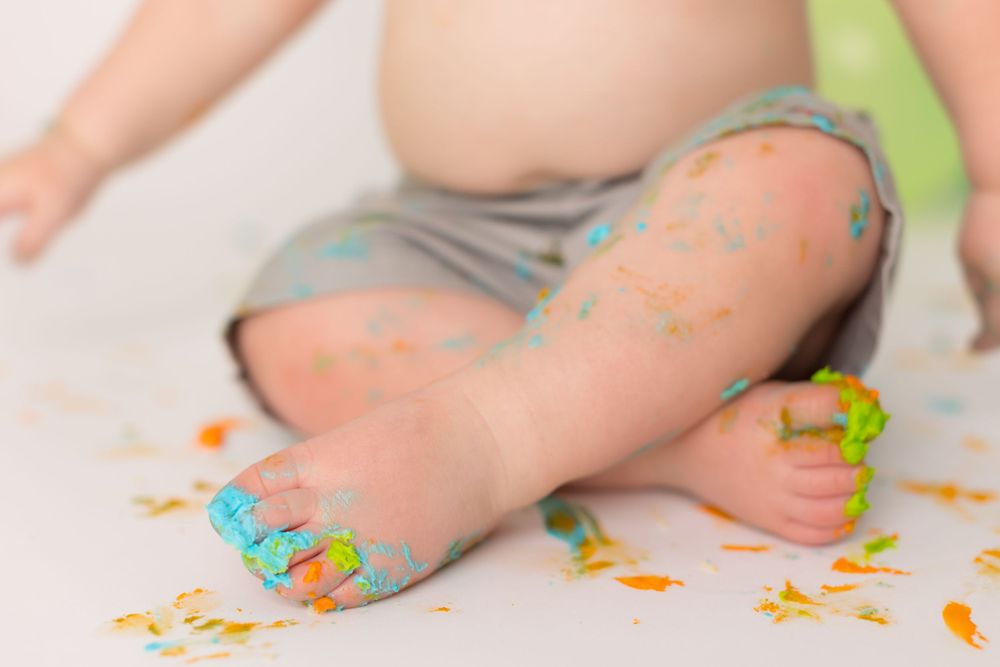 Close-up of baby's legs covered in blue and yellow cake frosting with sprinkles.
