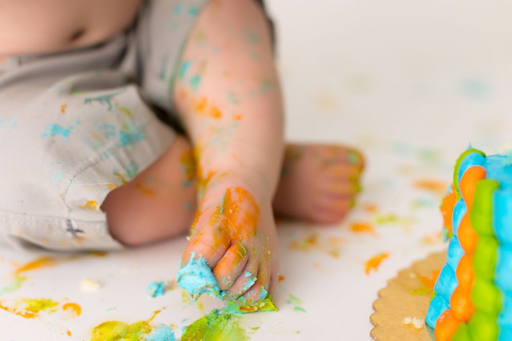 Close up of tiny hands playing with colorful birthday cake frosting and decorations.