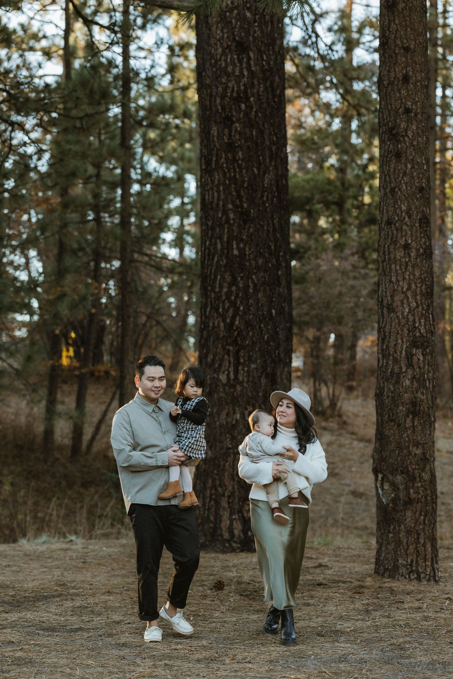 A family walks together among tall pine trees in a forest setting at dusk.