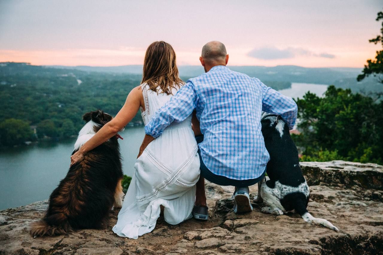 A couple and their dogs enjoy scenic lake view while sitting on rocky overlook.