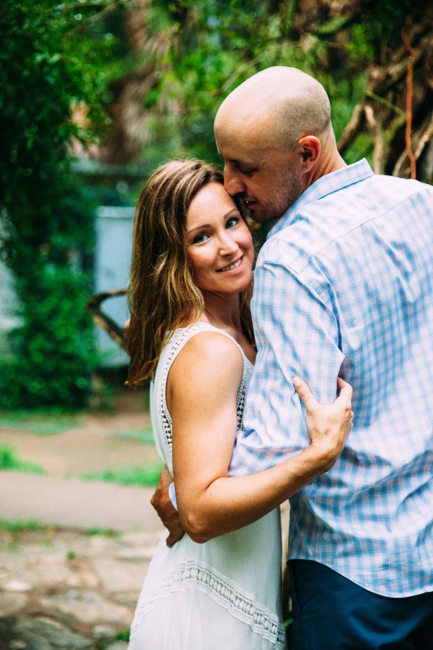 A romantic outdoor portrait of a couple embracing in a garden setting with lush green foliage in the background.
