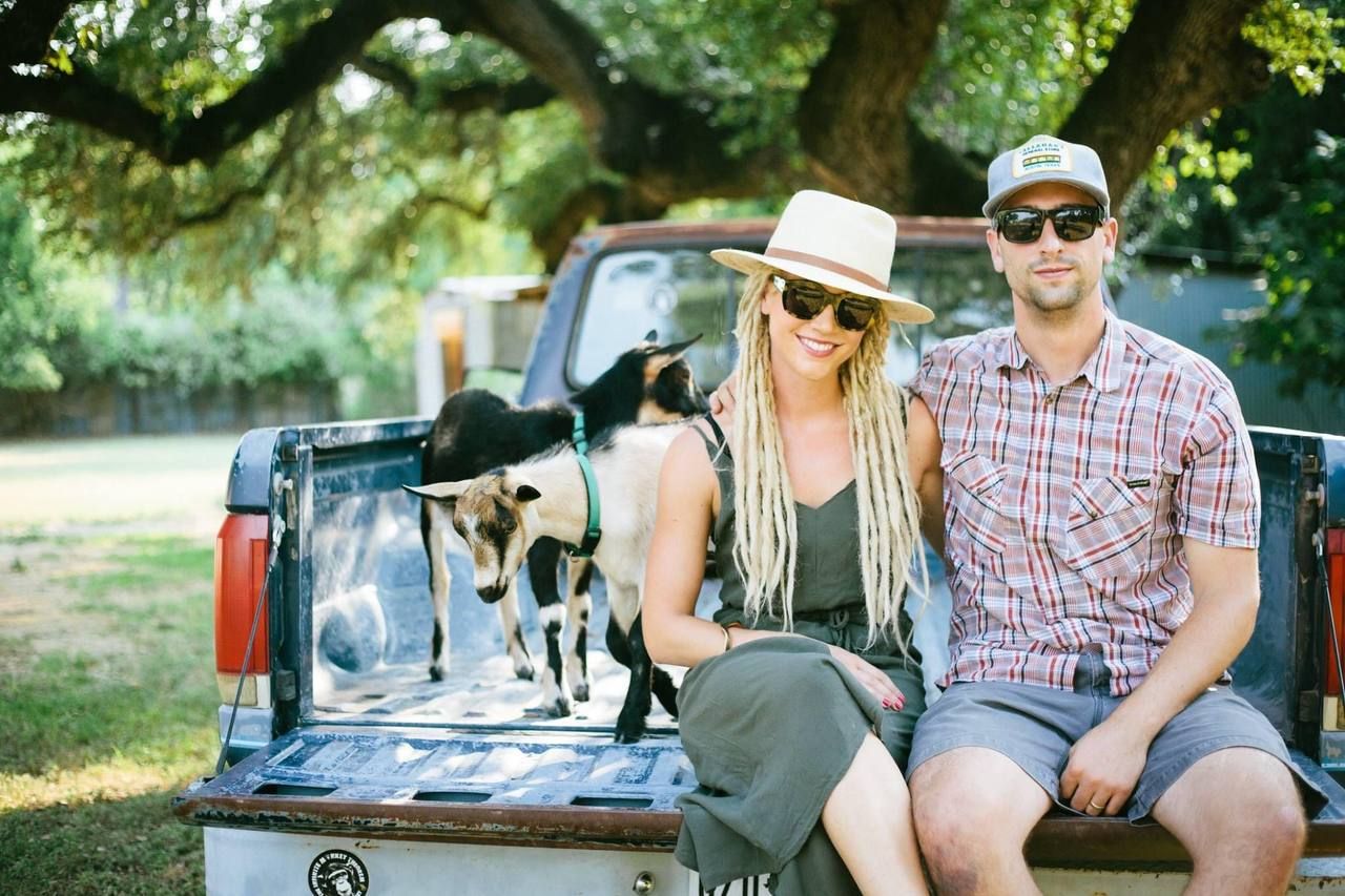 A casual couple sitting on the back of a pickup truck with their dogs on a sunny day.