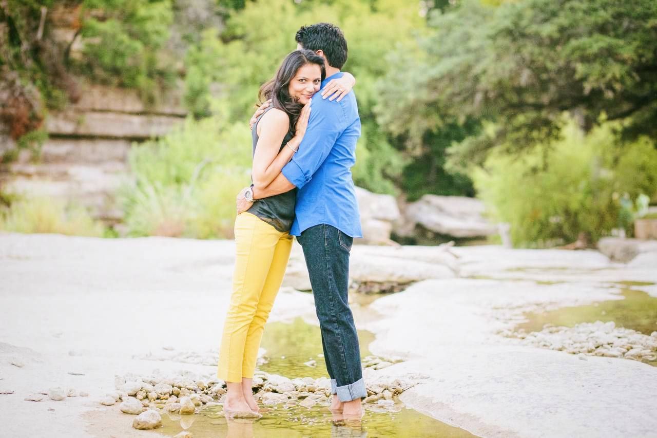 A couple embracing by a rocky creek wearing bright yellow and blue casual outfits.