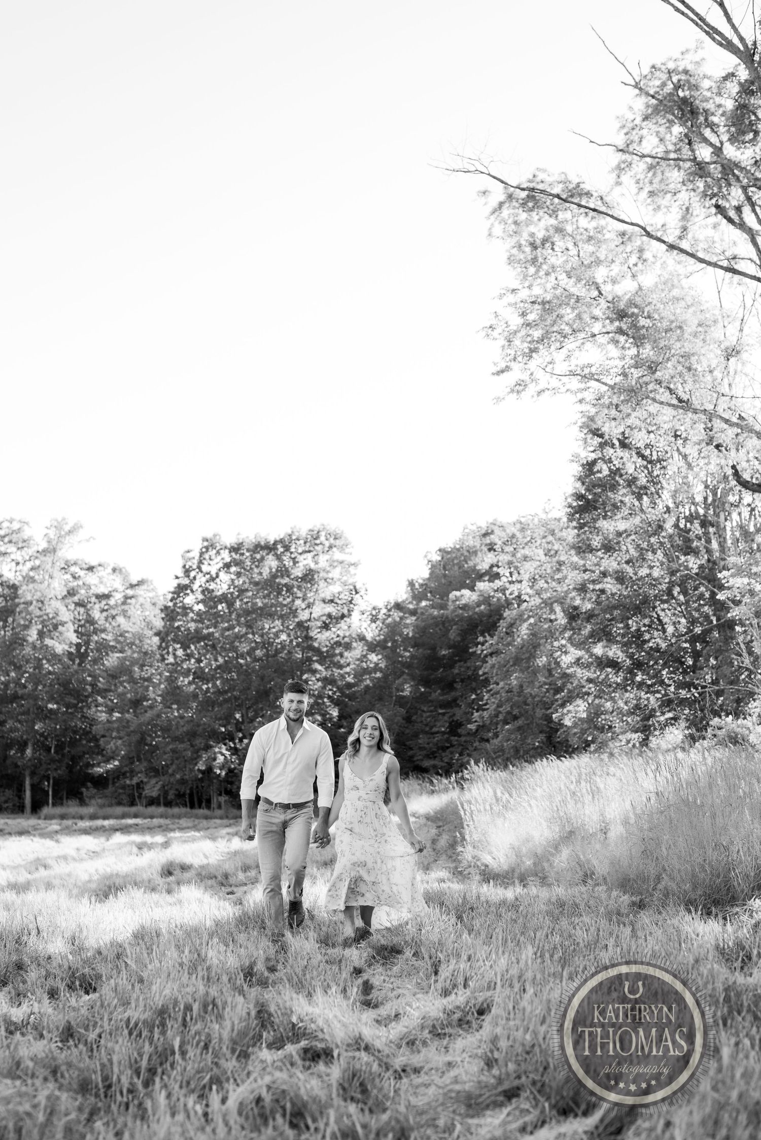 A couple walks hand in hand through a misty field in black and white photography.