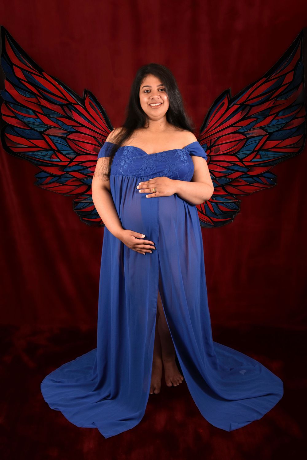 Maternity portraits with a royal blue flowing gown and decorative wing backdrop.
