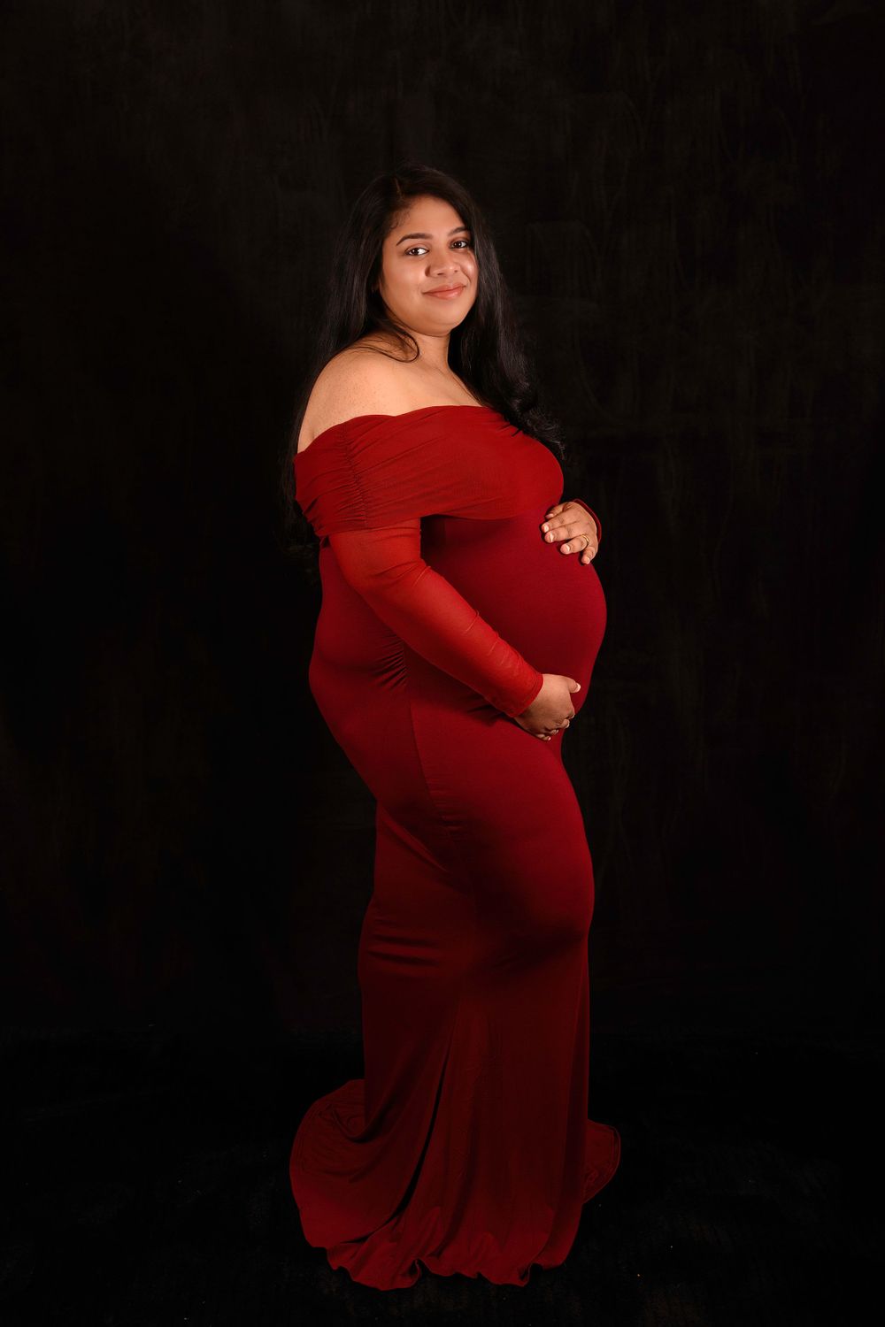 Moody maternity portraits in a red off-shoulder dress against a dark background.