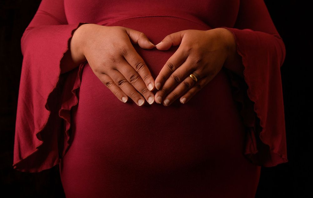 Close-up shots of hands lovingly placed on a pregnant belly in the shape of a heart in a red dress.