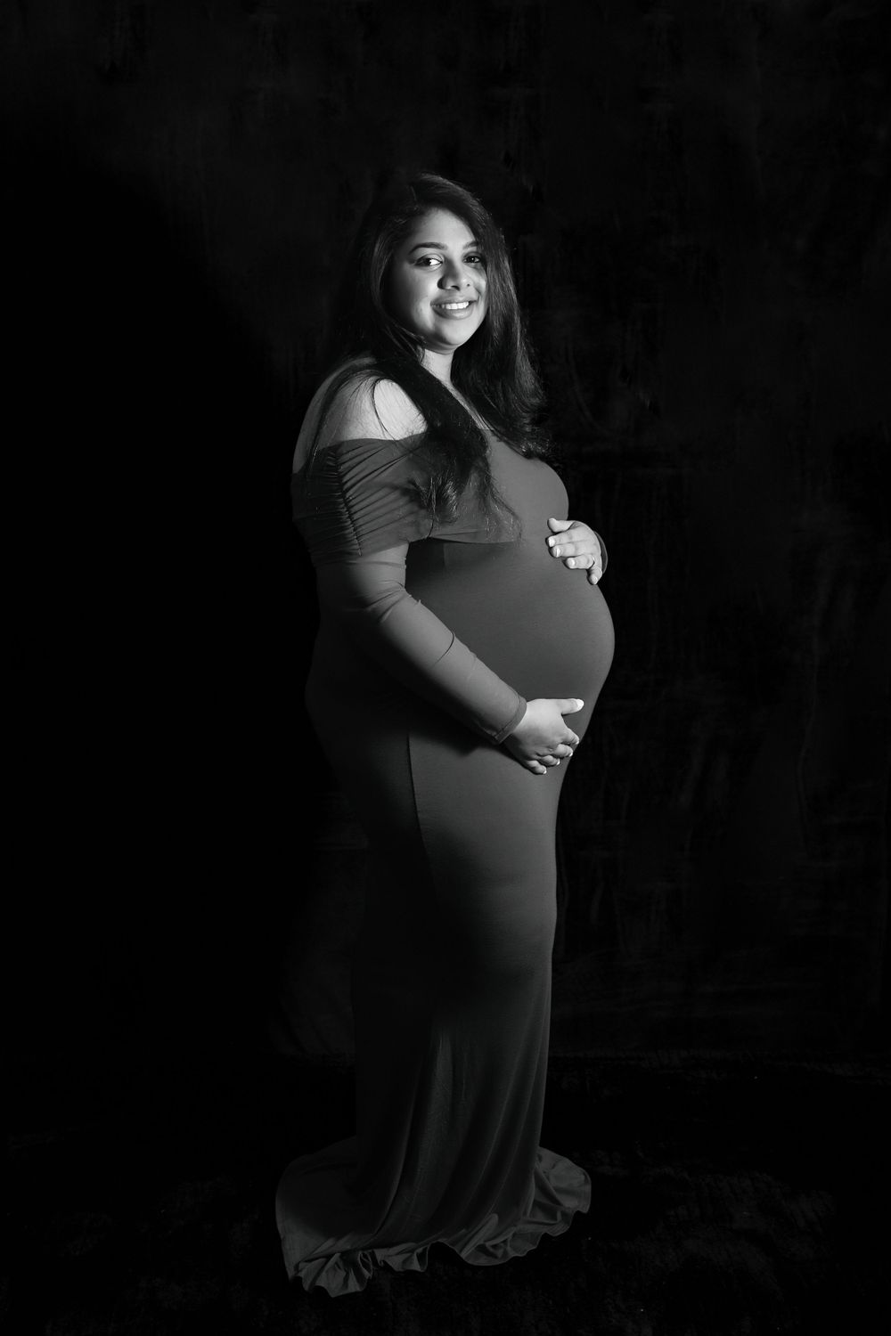Dramatic black and white maternity portraits showing an expectant mother in dark lighting.