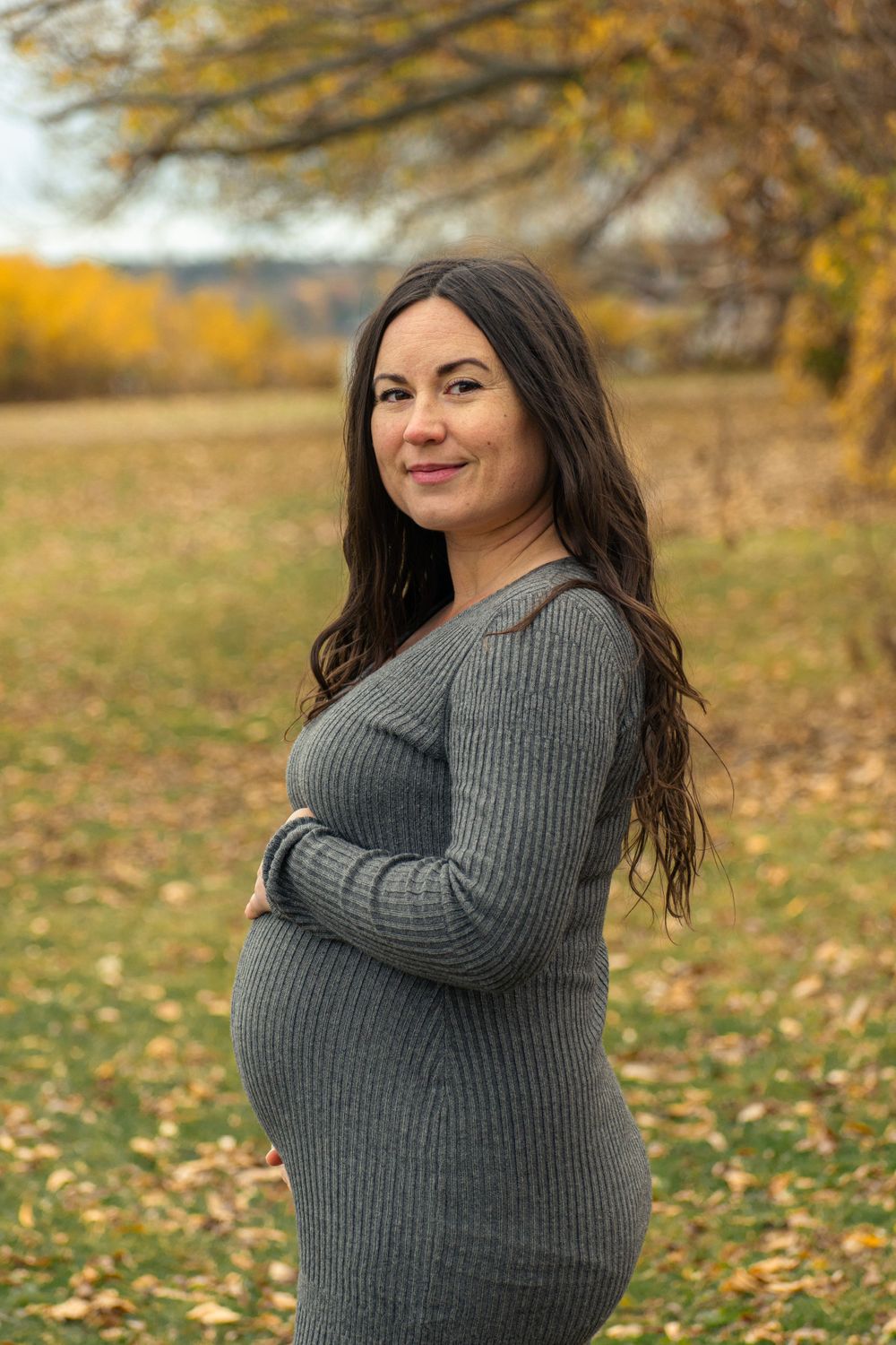 Outdoor maternity portrait with autumn colors and fallen leaves in background.