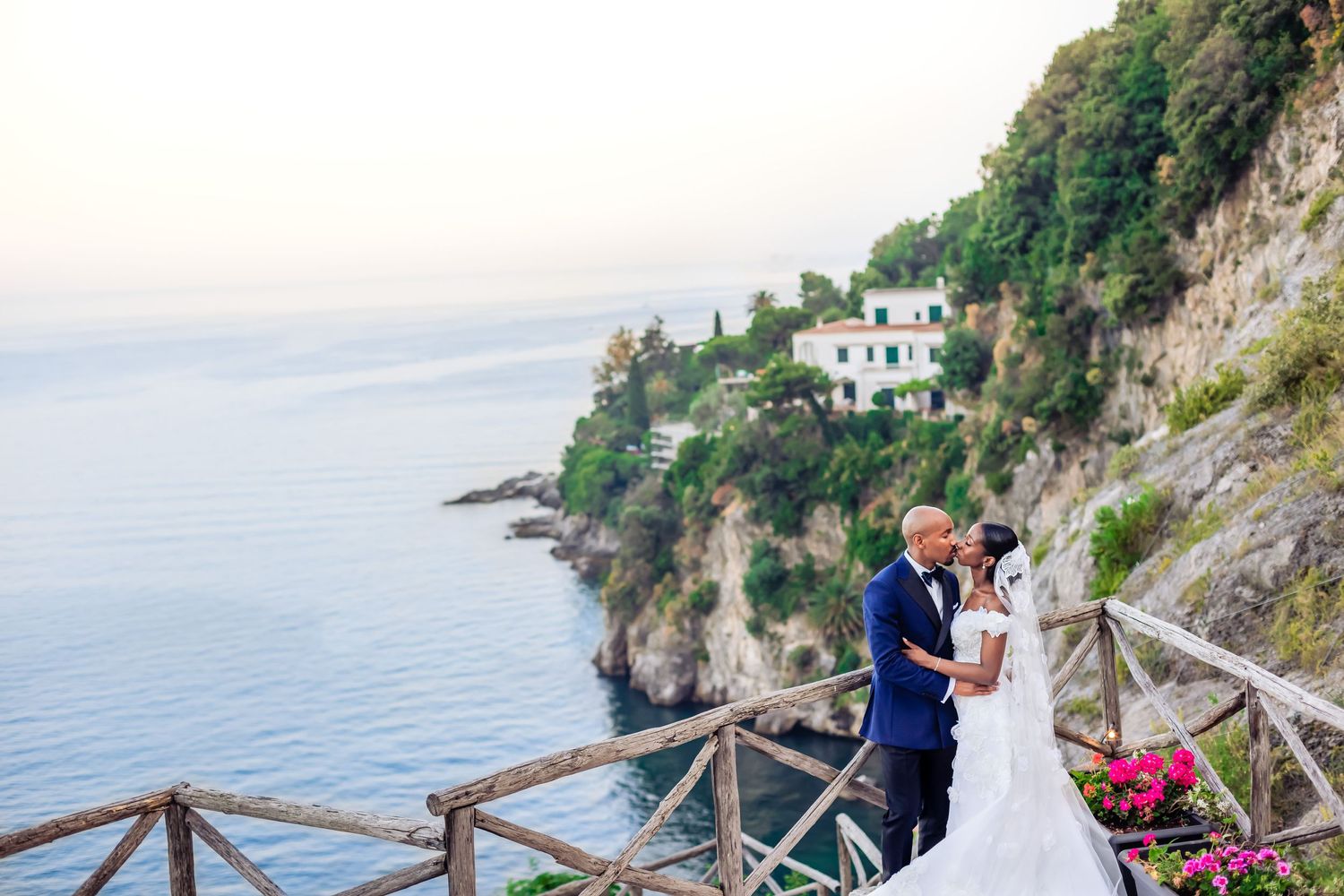 Couple shares romantic moment on coastal terrace overlooking Mediterranean cliffs and sea.