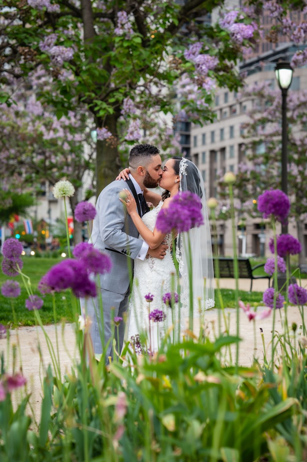 Couple shares intimate moment among purple flowers in urban garden setting.