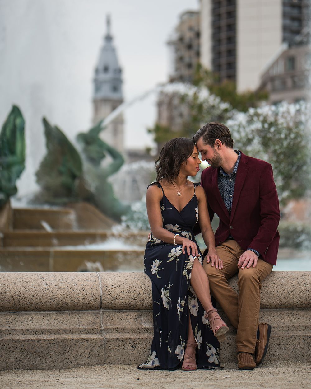 Couple sits intimately on fountain ledge with Philadelphia City Hall visible in background.